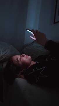 Girl doom scrolling her smartphone on a coach at night. Social network and phone addiction concept. Cozy home ambient light. vertical video