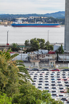 Cargo ship passing Martinez waterfront with vehicle staging lot in the foreground