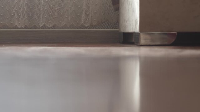 Robot vacuum cleaner drives along the wall and disappears behind the corner of the furniture. Automatic helper effectively cleans hard-to-reach places in a modern interior