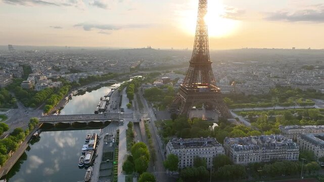 Aerial drone view of the streets of Paris, France, overlooking the famous Eiffel Tower and Champ de Mars at sunrise or sunset. Sun rays pass through the tower. Cinematic 4k. Europe from above
