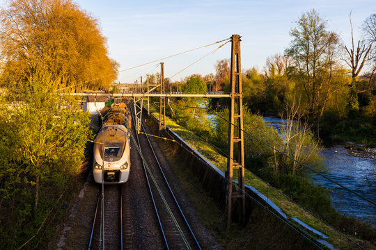 Nouvelle-Aquitaine TER regional train on the railway tracks alongside the Gave de Pau river crossing the city of Pau at sunset