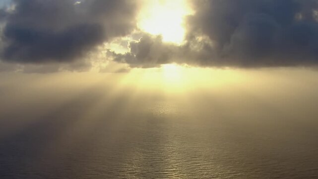 Majestic aerial view of sunbeams breaking through dark clouds over a calm sea at sunset