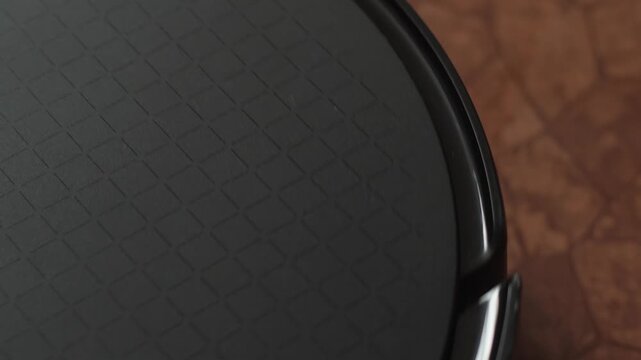 Close up of a male finger pressing the power button on a black robot vacuum cleaner. Smart gadget activating with a glowing power indicator for home cleaning.