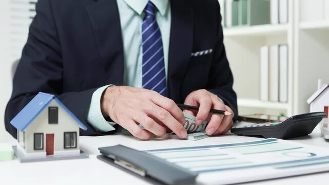 
Businessman shields tiny house with hand. Office desk holds coffee cup and pens. Professional demeanor suggests protection or security. Ideal for insurance, real estate, or financial services