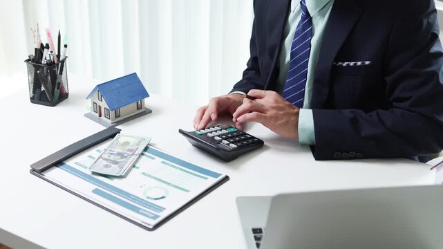 
Businessman shields tiny house with hand. Office desk holds coffee cup and pens. Professional demeanor suggests protection or security. Ideal for insurance, real estate, or financial services