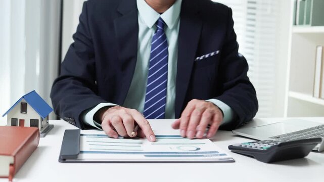 
Businessman shields tiny house with hand. Office desk holds coffee cup and pens. Professional demeanor suggests protection or security. Ideal for insurance, real estate, or financial services