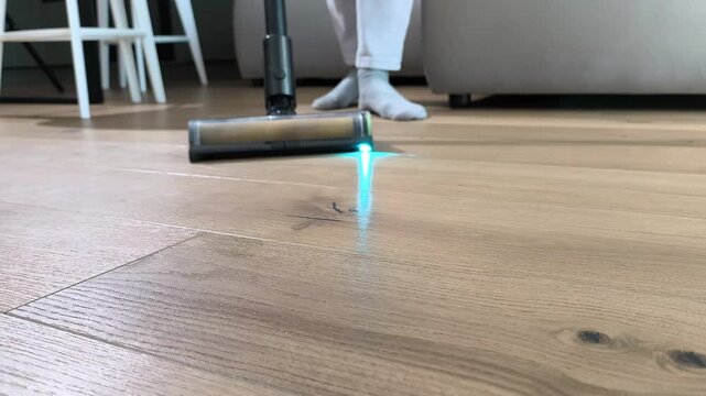 Close view shows rotating brush of vacuum cleaner removing dust from floor. Device head spins while cleaning wooden surface effectively. Home routine highlights detailed maintenance and