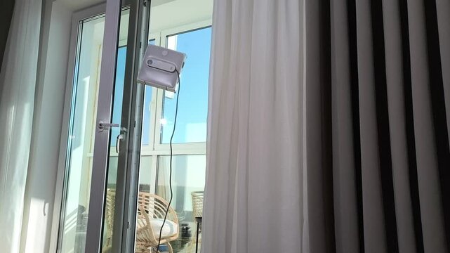 Robot cleaner washes window glass surface inside modern interior. Automated device moves steadily maintaining cleanliness and clarity. Spring cleaning concept supports organized domestic