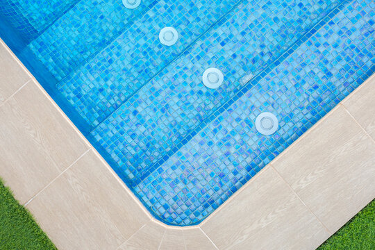 Overhead view of a luxury swimming pool corner with blue mosaic tiles, water jets, and surrounding deck with grass, minimal geometric composition - relaxation and luxury lifestyle concept