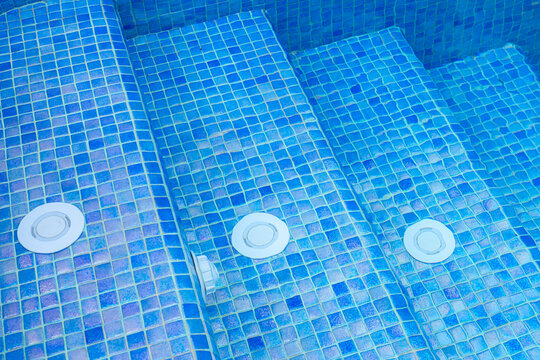Close-up of luxury swimming pool steps with blue mosaic tiles and built-in water jets, highlighting spa features, clean design, and relaxing atmosphere