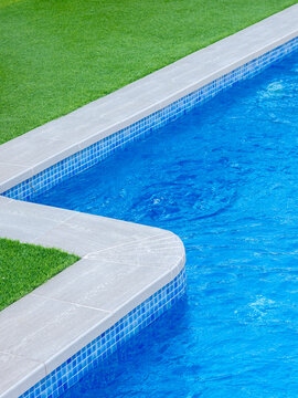 Close-up of a luxury swimming pool edge with blue water, mosaic tiles, and green grass, showcasing a modern outdoor design and relaxing summer atmosphere - relaxation and luxury lifestyle concept