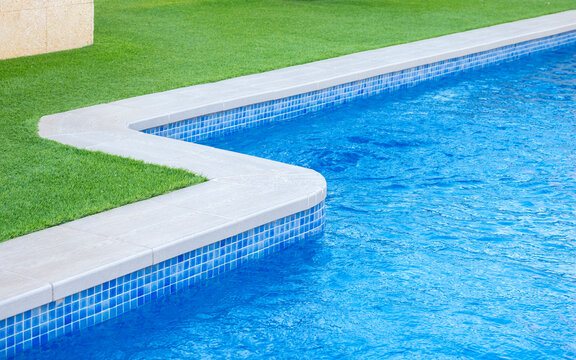 Close-up of a luxury swimming pool edge with blue water, mosaic tiles, and green grass, showcasing a modern outdoor design and relaxing summer atmosphere - relaxation and luxury lifestyle concept