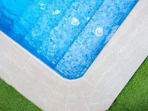Overhead view of a luxury swimming pool corner with blue mosaic tiles, bubbling water jets, and clean deck with grass - relaxation and luxury lifestyle concept