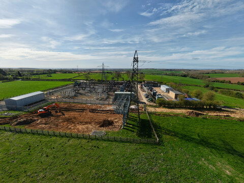 Aerial view of Coalville Substation featuring electrical infrastructure, power lines, and an orange excavator on a construction site surrounded by green fields Coalville, England, United Kingdom.