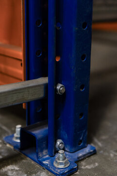 ll metal warehouse racks with blue vertical beams and orange safety brackets hold pallets and cardboard boxes. Some shelves feature green shuttle carriages. Clean industrial floor with green markings.