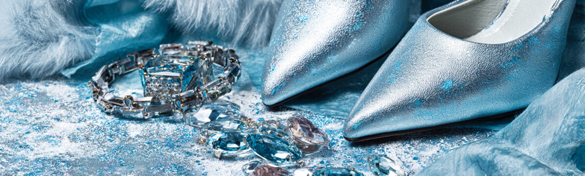 Close up of silver shimmer women shoes and jewelry placed on satin fabric. Elegant fashion still life for magazine backgrounds, luxury lifestyle branding and fashion advertising.