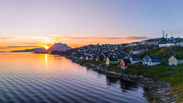 Aerial view of colorful houses along the rocky coastline with mountains in the background during a golden sunset Nuuk, Sermersooq Municipality, Greenland.