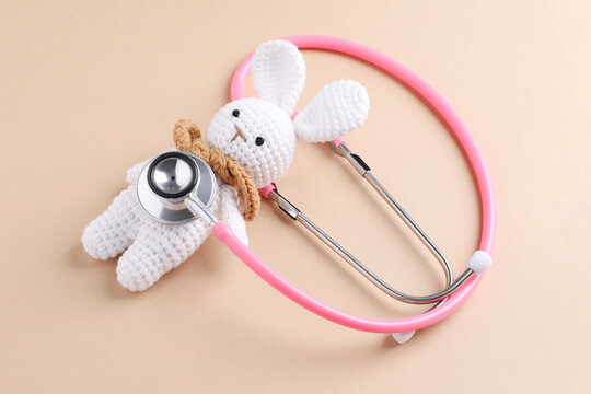 Children's doctor. Stethoscope and toy bunny on beige background, closeup