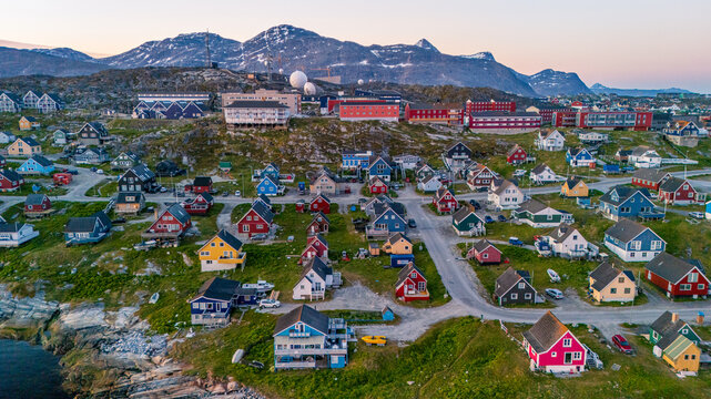 Aerial view of colorful houses and satellite dishes scattered across a rocky hillside with majestic mountains in the background during twilight in Nuuk, Sermersooq Municipality, Greenland.