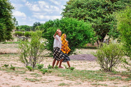 Two Basarwa women and a child walk through a sandy landscape with green bushes in Botswana
