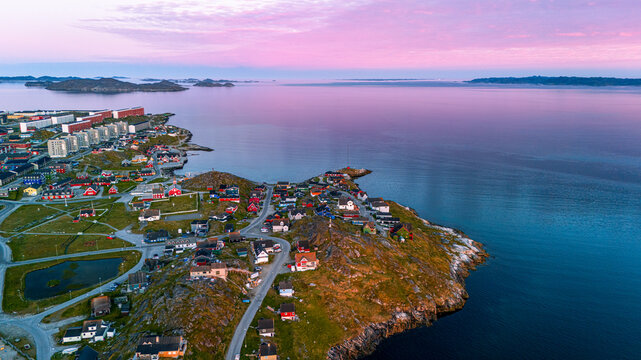 Aerial view of colorful houses on a rocky peninsula overlooking the calm sea under a vibrant sunset sky Nuuk, Sermersooq Municipality, Greenland.