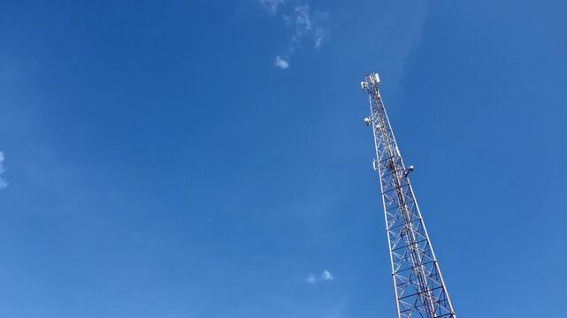 A tall metal lattice telecommunication tower stands high against a clear blue sky during a bright day
