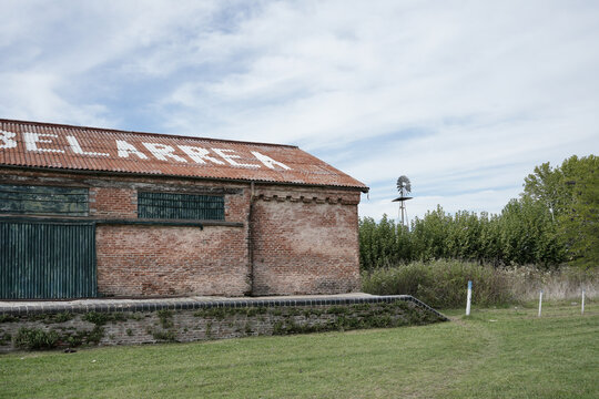 URIBELARREA, ARGENTINA - APRIL 11, 2026: Rural landscape featuring the brick facade of the old station and a traditional windmill in the background.