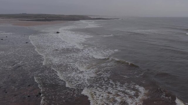 Aerial view of ocean waves hitting sandy beach coastline in Scotland, cinematic 5 second clip