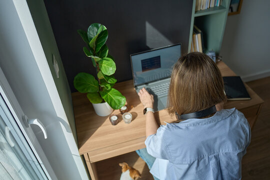 Woman using laptop while sitting at desk in home office, viewed from above