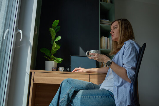 Woman sitting with mug at desk near laptop in home office