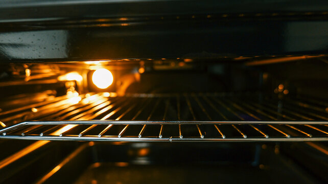 Inside view of a clean oven with a glowing light and metal racks