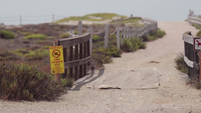A walkway with a sign warning people of the hazards of water at Border Field State Park due to Tijuana River pollution