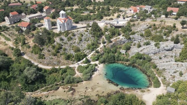 Forward descending drone uncovers the turquoise Cetina spring beside an Orthodox church on the slopes of Dinara in Croatia.