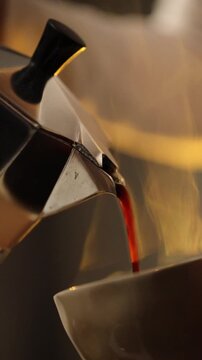 Fresh coffee is poured from a moka pot into a cup in a home kitchen.