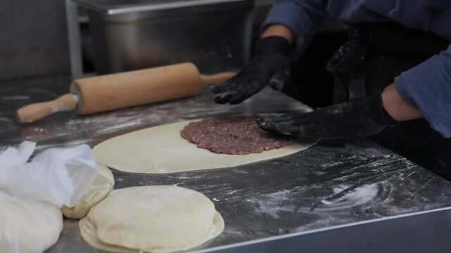 A female chef prepares traditional fried pastries in a professional restaurant kitchen, shaping dough and cooking fresh food by hand.