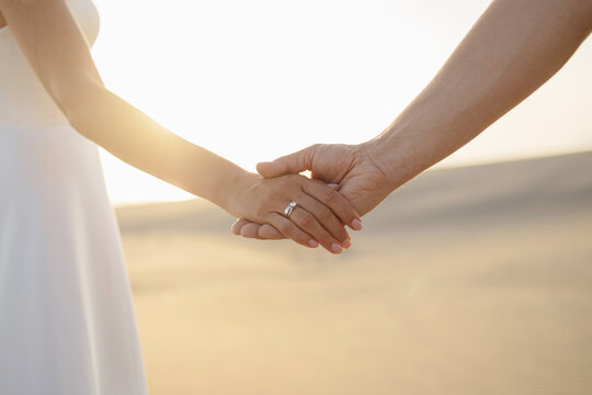 Couple holding hands with engagement wedding ring at sunset