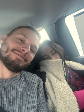 ugc. A selfie of a smiling husband with his sleeping wife in a car 