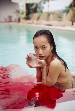 Asian woman wearing a red dress holds a crystal ball in the pool
