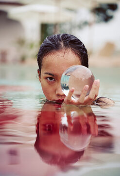 Asian woman wearing a red dress holds a crystal ball in the pool