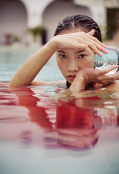 Asian woman wearing a red dress holds a crystal ball in the pool
