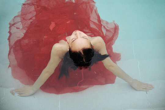 Asian woman in a red tulle dress is in the swimming pool