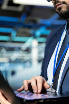 Close up of programmer in data center typing on laptop keyboard, upgrading rigs. IT staff member using notebook in modern server farm to enhance operational effectiveness of hardware