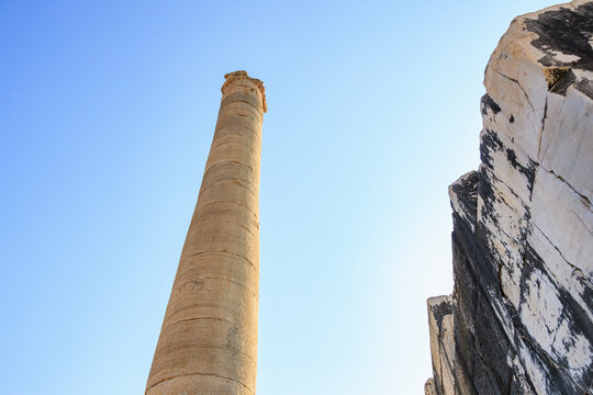 Ancient stone column under clear blue sky amid ruins