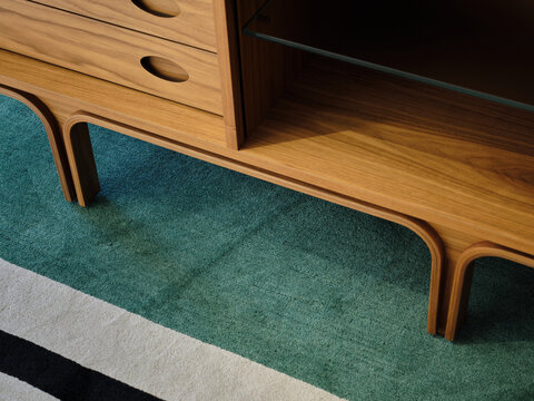 Detail of wooden sideboard with colourful stripped rug