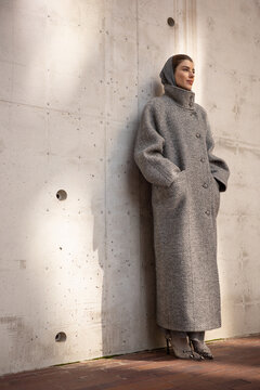 Woman in Textured Coat Leaning on Concrete Wall