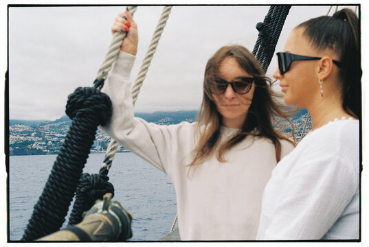 Two Women on Boat Deck Holding Ropes with Madeira Coastline Behind