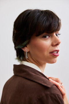 Woman with short hair looks back while wearing a brown jacket