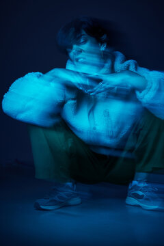 Person sitting in blue light with blurred motion effect in a dar