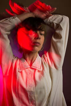 Woman poses with hands raised under colored lights in a studio