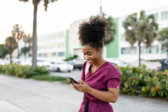 Young Woman in Medical Uniform Walking on a Street Using Phone Smiling